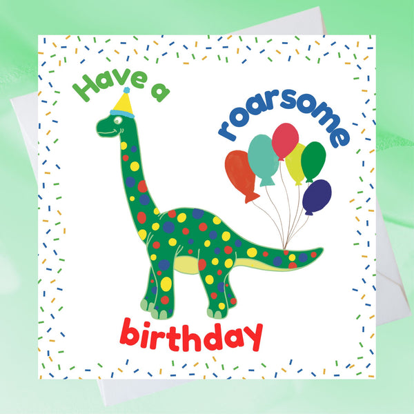 A Mary Martha & Meg child’s birthday card featuring a friendly green dotty dinosaur with party balloons tied to its tail. The text reads, ‘Have a roarsome birthday.’ The crisp white card has a colourful confetti border. A white envelope peeps out behind the card. The card is placed on a pale green background.
