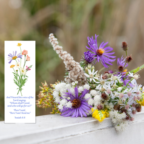 A gorgeous Mary, Martha & Meg bookmark with a delicate bouquet of pastel wildflowers. The bookmark is placed on a windowsill next to a bunch of flowers, the purple aster echoing the lilac aster in Meg’s design. The bookmark quotes the Bible verse, ‘And I heard the voice of the Lord saying, “Whom shall I send, and who will go for us?” Then I said, “Here I am! Send me.”’ Isaiah 6:8. A perfect reminder that we are all called to serve the Lord.
