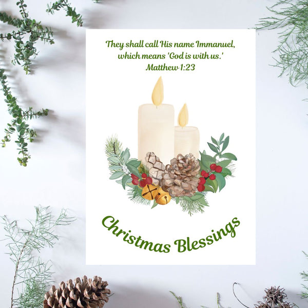 A white Mary, Martha & Meg Christmas Greeting card featuring two lit candles resting on a Christmas wreath of holly berries, pine cones, Christmas bells and foliage. The Bible verse above the design reads, "They shall call His name 'Immanuel' which means 'God is with us.' Matthew 1:23" The greeting, ‘Christmas Blessings’ is also included. The white card is photographed on a background of delicate green foliage and pine cones.