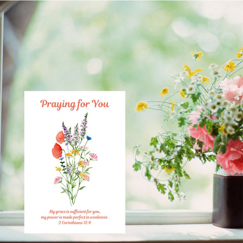 A thoughtful card with the words, ‘Praying for You’ above a lovely bouquet of red poppies and other delicate flowers. The Bible verse underneath the flowers reads, “My grace is sufficient for you, my power is made perfect in weakness.” 2 Corinthians 12:9. The A6 card is pictured on a windowsill next to a vase of flowers. This Mary, Martha & Meg card serves as a lovely reminder of how we can draw closer to God in prayer, receiving the gentle quietness we can have in trusting our heavenly Father’s promises.