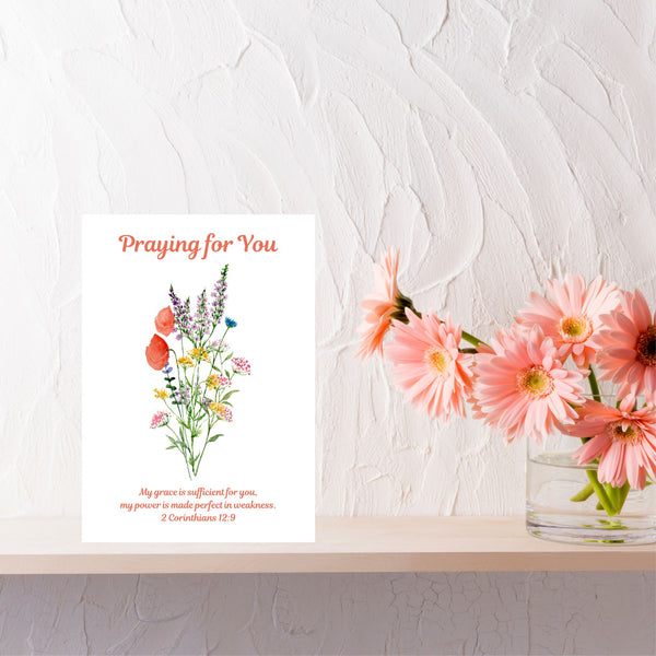 A thoughtful card with the words, ‘Praying for You’ above a lovely bouquet of red poppies and other delicate flowers. The Bible verse underneath the flowers reads, “My grace is sufficient for you, my power is made perfect in weakness.” 2 Corinthians 12:9. The A6 card is pictured on a shelf next to a vase of peach flowers. This Mary, Martha & Meg card serves as a lovely reminder of how we can draw closer to God in prayer, receiving the gentle quietness we can have in trusting our heavenly Father’s promises.