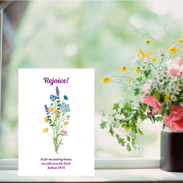 A Mary Martha & Meg A6 white card featuring the word ‘Rejoice’ above a floral bouquet of pretty wildflowers. Underneath the flowers is the Bible verse, “As for me and my house, we will serve the Lord.” Joshua 24:15. The card is pictured on a white windowsill next to a vase of flowers. This card can be displayed in your home as a daily reminder to serve the Lord in all we do. It is also a lovely greetings card to send to a friend moving into a new home.