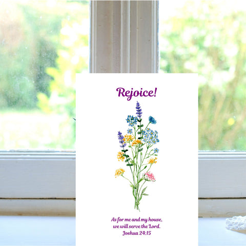 A Mary Martha & Meg A6 white card featuring the word ‘Rejoice’ above a floral bouquet of pretty, colourful wildflowers. Underneath the flowers is the Bible verse, “As for me and my house, we will serve the Lord.” Joshua 24:15. The card is pictured on a white windowsill. This card can be displayed in your home as a daily reminder to serve the Lord in all we do. It is also a lovely greetings card to send to a friend moving into a new home.