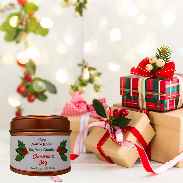 A Mary, Martha & Meg Christmas soy wax candle presented in a ‘rose gold’ lidded tin. The candle title, ‘Christmas Joy,’ is written in red text. The candle fragrance is ‘Red Berry and Holly,’ a beautiful aroma of fruit and berries which evokes the nostalgia of Christmas. The background of this photo shows four small Christmas presents, wrapped with bows and decorated with holly and red berries.