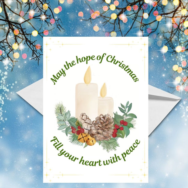 A white Christmas Greeting card featuring two lit candles resting on a Christmas wreath of holly berries, pine cones, golden Christmas bells and foliage. The Christmas scene is framed by the greeting, ‘May the hope of Christmas fill your heart with peace.’ A white envelope rests behind the car. This Mary, Martha & Meg Christmas card is photographed on a blue Christmassy background with twigs decorated with small, pastel-coloured lights.