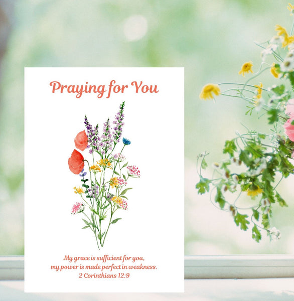 A thoughtful card with the words, ‘Praying for You’ above a lovely bouquet of red poppies and other delicate flowers. The Bible verse underneath the flowers reads, “My grace is sufficient for you, my power is made perfect in weakness.” 2 Corinthians 12:9. The A6 card is pictured on a windowsill next to a vase of flowers. This Mary, Martha & Meg card serves as a lovely reminder of how we can draw closer to God in prayer, receiving the gentle quietness we can have in trusting our heavenly Father’s promises