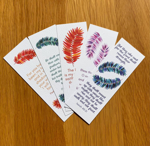 5 bookmarks with feather designs on a light brown wooden background