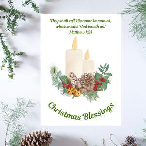 A white Mary, Martha & Meg Christmas Greeting card featuring two lit candles resting on a Christmas wreath of holly berries, pine cones, Christmas bells and foliage. The Bible verse above the design reads, "They shall call His name 'Immanuel' which means 'God is with us.' Matthew 1:23" The greeting, ‘Christmas Blessings’ is also included. The white card is photographed on a background of delicate green foliage and pine cones.