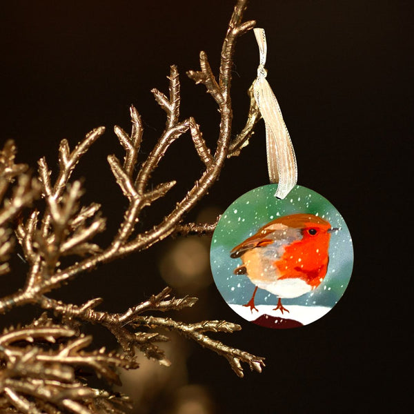 A photograph of a Mary, Martha & Meg pretty hanging decoration featuring a traditional winter robin perched on a snowy branch. The decoration is hung by a silver ribbon, ready to be placed on your Christmas tree, popped in with a Christmas card, or even added to a Christmas bouquet of flowers. The decoration is seen hanging from a golden branch against a dark background.