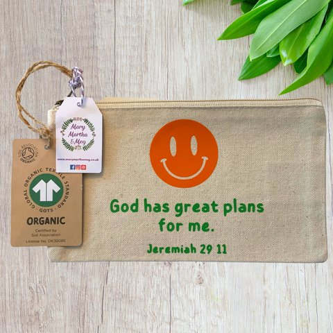 A Mary, Martha & Meg organic, natural, canvas zip pouch featuring the words ‘God has great plans for me. Jeremiah 29:11.’ Above this is an orange smiley face. The design has been hand-printed. A Mary, Martha & Meg tag hangs from the zip, as well as a label showing the organic credentials of the zip pouch. The zip pouch is pictured on a wooden table with green leaves in the top right corner. A great gift which can be posted through a letterbox.