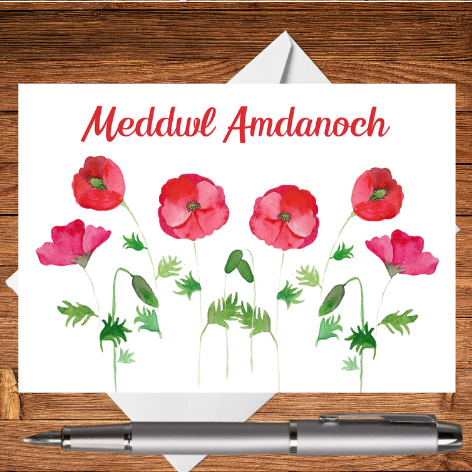 A classic Mary, Martha & Meg thinking of you greetings card in Welsh – Meddwl Amdanoch. This cerdyn cyfarch features red poppies (pabïau goch), which have been hand-painted using watercolours. The edges of a crisp white envelope can be seen behind the card, which rests on a wooden writing surface. A silver pen has been placed beneath the card. A perfect card to remind a Welsh friend you are thinking of them.