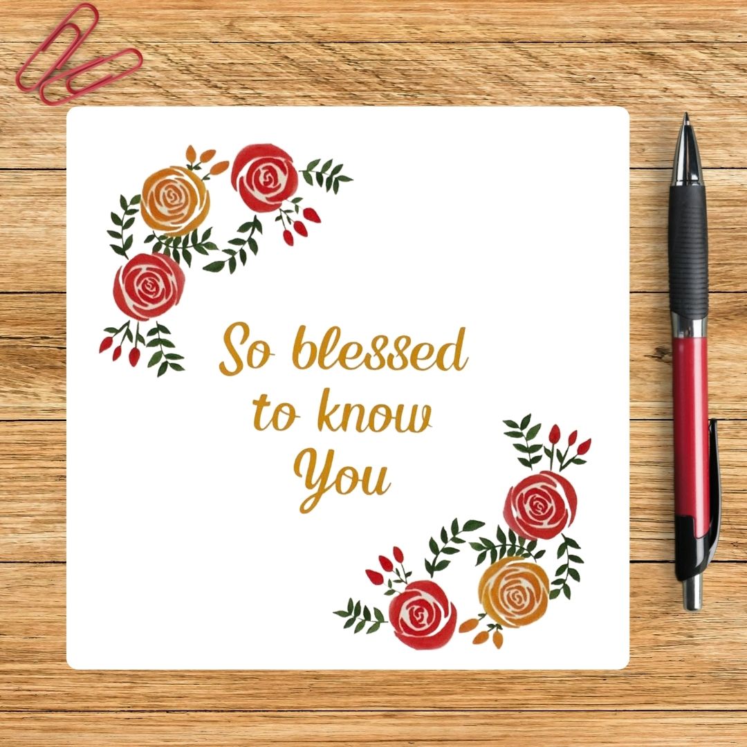 A Greeting Card with the text 'So Blessed To Know You' surrounded with roses and foliage. The card is on a wooden background  with red paperclips and next to a red pen.