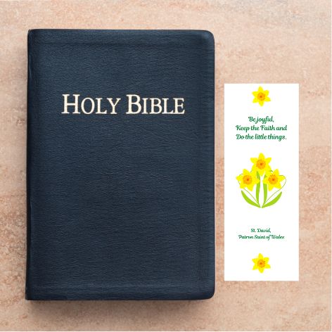 A white bookmark with the words ‘Be Joyful, Keep the faith and Do the little things.’ Above the green text is a single golden daffodil. Beneath the text are three beautiful daffodils. The words St. David, Parton Saint of Wales are included, with another daffodil underneath this. This Mary, Martha & Meg bookmark is pictured next to a Black Holy Bible.