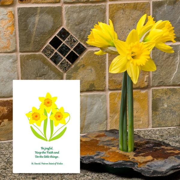 A bright, eye-catching card of three golden daffodils features the last words of David, Patron Saint of Wales, “Be Joyful. Keep the Faith. Do the little things.” It is a lovely reminder to serve each other in the little things we do, no matter how small. This Mary, Martha & Meg card is pictured next to golden daffodils standing upright in a piece of stone, against a tiled stone background.