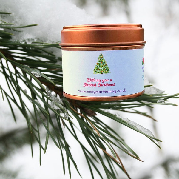 Mary, Martha & Meg 'Winter Forest' Soy Wax Candle balanced on a fir tree branch. A wintery Christmas Tree Fragrance. The back of the candle has a watercolour Christmas Tree design and a Christmas greeting in red which reads, 'Wishing you a Blessed Christmas.'